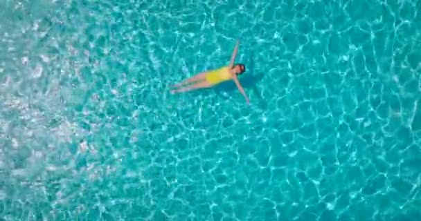 黄色の水着を着た女性のトップダウンビューは プールで彼女の背中に横たわっている スローモーション リラックスしたコンセプト 夏のライフスタイル — ストック動画