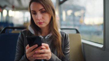 Toplu taşıma. Tramvayda akıllı telefon kullanan, arkadaşlarıyla mesajlaşan bir kadın, ağır çekim. Şehir, şehir, ulaşım.