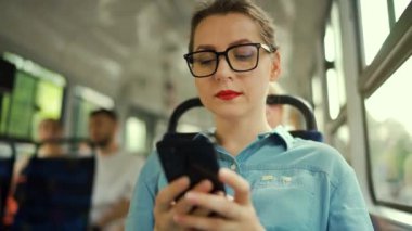 Toplu taşıma. Tramvaydaki gözlüklü kadın akıllı telefon konuşmaları yapıyor ve arkadaşlarıyla mesajlaşıyor. Şehir, şehir, ulaşım. Yavaş çekim