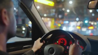 Gece şehrinin sokaklarında araba süren bir adam. Arabanın camında bir parlama var. Arabanın arka koltuğundan bak..