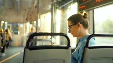 Toplu taşıma. Tramvaydaki gözlüklü kadın akıllı telefon konuşmaları ve arkadaşlarıyla mesajlaşmalar, arka plan, ağır çekim. Şehir, şehir, ulaşım.