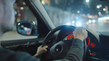 Gece şehrinin sokaklarında araba süren bir adam. Arabanın camında bir parlama var. Arabanın arka koltuğundan bak..