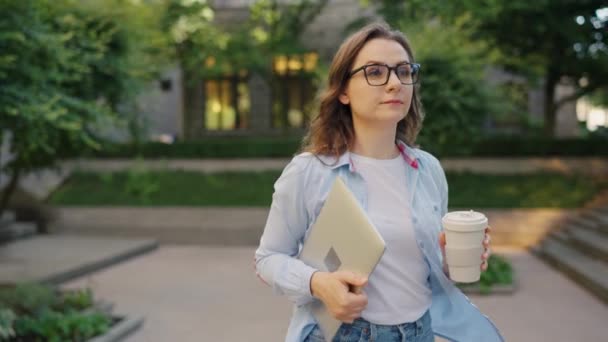 オフィスで仕事の日の後にノートパソコンとコーヒーを手に街を歩くケアフリービジネス女性 スローモーション — ストック動画