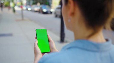 Kadın cadde boyunca gidiyor ve akıllı telefon kullanıyor. Yeşil ekran, arka görüş, yavaş çekim. İletişim, iş günü, yoğun yaşam konsepti.
