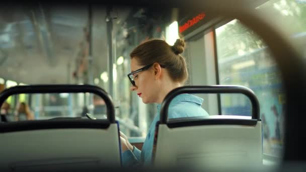 公共交通 戴眼镜的女人在有轨电车里用智能手机和朋友聊天和发短信 回头看 慢动作 — 图库视频影像