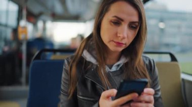 Toplu taşıma. Tramvayda akıllı telefon kullanan, arkadaşlarıyla mesajlaşan bir kadın, ağır çekim. Şehir, şehir, ulaşım.