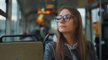 Public transport. Woman in glasses riding a tram in the city, slow motion. City, urban, transportation.