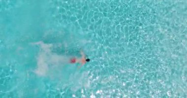 Bir adamın havuza dalıp, yavaş çekimde yüzdüğü tepeden aşağı bir manzara.