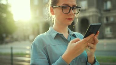 Gün batımında dışarıda dikilirken akıllı telefon kullanan bir kadın. İletişim, iş günü, yoğun yaşam konsepti. Yavaş çekim
