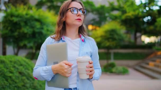 オフィスで仕事の翌日 ラップトップとコーヒーを手に通りに立っているケアフリーのビジネス女性 オービットショット — ストック動画