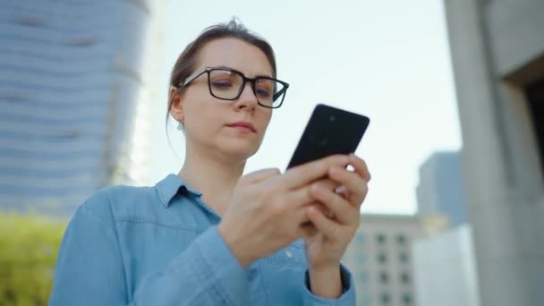 Mujer Caucásica Gafas Encuentra Centro Ciudad Uso Teléfonos Inteligentes Rascacielos — Vídeo de stock