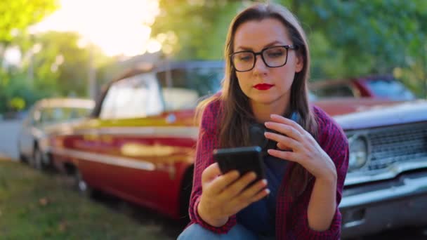 Woman Headphones Crouched Next Red Vintage Car Using Smartphone Blooming — Stock Video