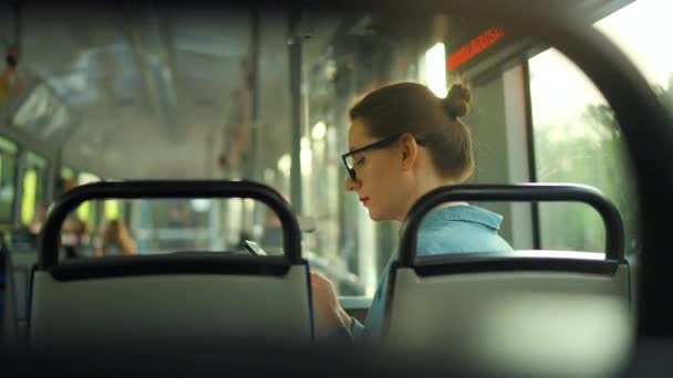 公共交通 坐在电车里戴眼镜的女人用智能手机和朋友聊天和发短信 后视镜 — 图库视频影像
