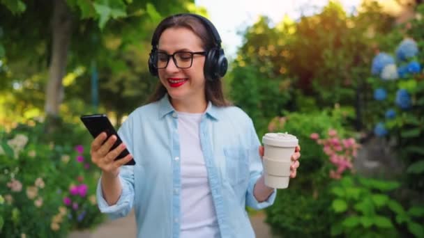 Wanita Bahagia Berkacamata Dan Headphone Dengan Kopi Dan Smartphone Tangannya — Stok Video