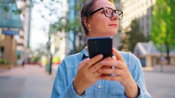 Biała Kobieta Okularach Stoi Pośrodku Miasta Używa Smartfona Zwolnionego Tempa — Wideo stockowe