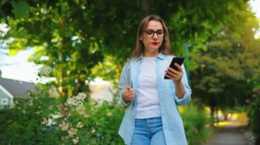 Dizüstü bilgisayarı ve akıllı telefonu olan mutlu bir kadın çiçek açan bahçede ya da işten sonra yeşil sokakta yürüyor, ağır çekimde..