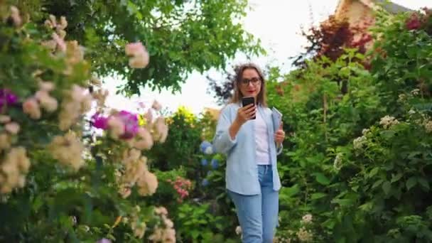 快乐的女人 手里拿着笔记本电脑和智能手机 下班后漫步在繁华的花园或绿色的街道上 — 图库视频影像