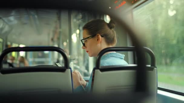 公共交通 戴眼镜的女人在有轨电车里用智能手机和朋友聊天和发短信 回头看 慢动作 — 图库视频影像