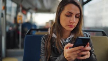 Toplu taşıma. Tramvayda akıllı telefon kullanan, arkadaşlarıyla mesajlaşan bir kadın, ağır çekim. Şehir, şehir, ulaşım.