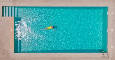 Sarı mayolu bir kadının havuzda sırt üstü yatışı. Ağır çekim. Rahatlatıcı konsept, yaz yaşam tarzı