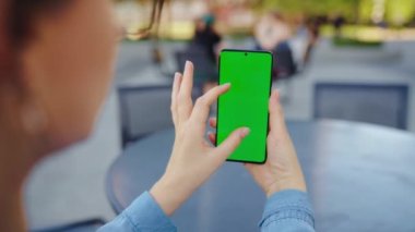 Kadın sokakta dikiliyor ve yeşil ekranlı, arka görüşlü akıllı telefon kullanıyor. İletişim, iş günü, yoğun yaşam konsepti.