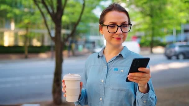 Běloška Brýlích Stojí Ulici Používá Smartphone Pije Kávu Mrakodrapy Jsou — Stock video