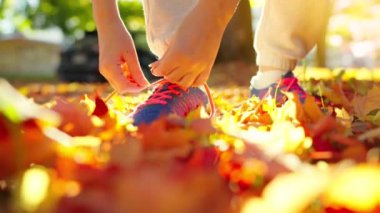 Gün batımında koşarken ya da yürürken ayakkabı bağı bağlayan bir kadın. Sonbahar sarı yaprakları. Yavaş çekim.