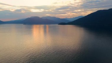 Akşamları Vancouver 'ın kuzeyindeki deniz manzarası. Gün batımı bulutlu gökyüzü ve dağların siluetleri. British Columbia, Kanada.