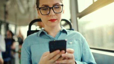 Toplu taşıma. Tramvaydaki gözlüklü kadın akıllı telefon konuşmaları yapıyor ve arkadaşlarıyla mesajlaşıyor. Şehir, şehir, ulaşım. Yavaş çekim