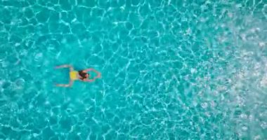 Top down view of a woman in yellow swimsuit swimming in the pool. Summer lifestyle
