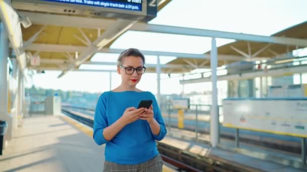 妇女在公交车站上行走 使用智能手机 等待火车 — 图库视频影像