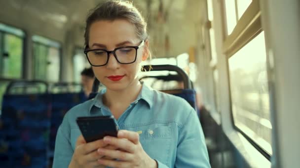 公共交通機関だ スマートフォンのチャットや友人とのテキストメッセージを使用してトラムのメガネの女性 スローモーション — ストック動画