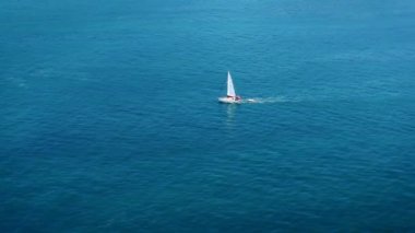Yelkenlinin açık mavi bir denizde beyaz dalgalarla yüzüşünü gösteren hava görüntüleri. Drone 'dan deniz burnu. Seyahat videosu