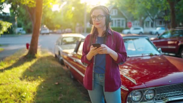 Γυναίκα Ακουστικά Στέκεται Εξωτερικούς Χώρους Κοντά Στο Κόκκινο Vintage Αυτοκίνητο — Αρχείο Βίντεο