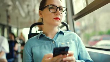 Toplu taşıma. Tramvaydaki gözlüklü kadın akıllı telefon konuşmaları yapıyor ve arkadaşlarıyla mesajlaşıyor. Şehir, şehir, ulaşım. Yavaş çekim