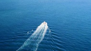 Derin mavi bir denizde beyaz dalgalı hızlı bir teknenin havadan görüntüsü. Drone 'dan deniz burnu. Seyahat videosu
