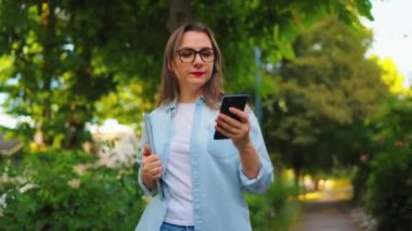 Dizüstü bilgisayarı ve akıllı telefonu olan mutlu bir kadın çiçek açan bahçede ya da işten sonra yeşil sokakta yürüyor..