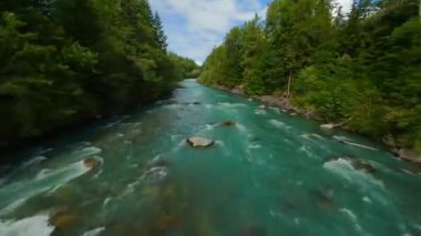 FPV insansız hava aracı hızlı akan nehir üzerinde su ve demiryolu hattına yakın bir yerde uçuyor. Etrafı çam ormanlarıyla çevrili. Whistler, British Columbia, Kanada yakınlarında çekilmiş..