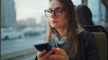 Toplu taşıma. Tramvayda akıllı telefon kullanan, arkadaşlarıyla mesajlaşan bir kadın. Şehir, şehir, ulaşım.