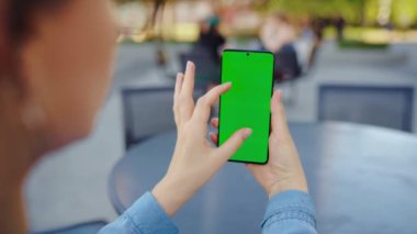 Kadın sokakta dikiliyor ve yeşil ekranlı, arka görüşlü akıllı telefon kullanıyor. İletişim, iş günü, yoğun yaşam konsepti.