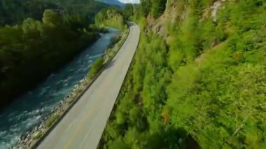 FPV drone flight over the road and the fast moving river with rapids, close to the water. Surrounded by Pine Forest. Taken near Whistler, British Columbia, Canada.