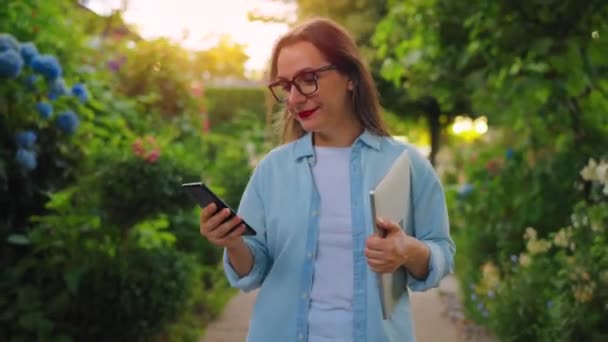 Szczęśliwa Kobieta Laptopem Smartfonem Rękach Spacerując Kwitnącym Ogrodzie Lub Zielonej — Wideo stockowe