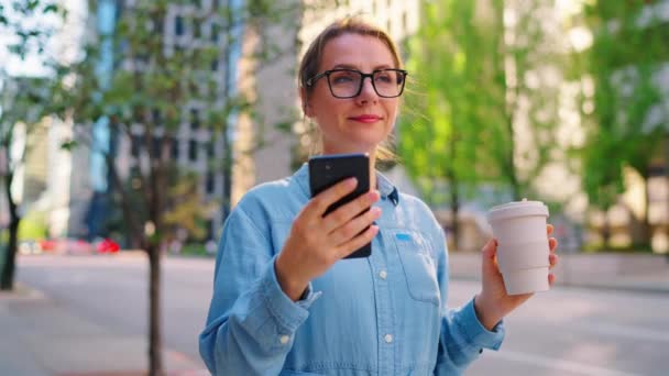 Vit Kvinna Glasögon Står Gatan Använder Smartphone Och Dricker Kaffe — Stockvideo
