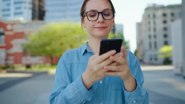 戴眼镜的白人妇女正在城市里走来走去 使用智能手机 摩天大楼在后面 工作日 忙碌的生活理念 慢动作 — 图库视频影像