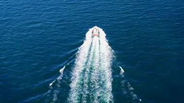 Derin mavi bir denizde beyaz dalgalı hızlı bir teknenin havadan görüntüsü. Drone 'dan deniz burnu. Seyahat videosu