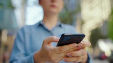 Gözlüklü beyaz kadın şehirde dolanıyor ve akıllı telefon kullanıyor. Arka planda gökdelenler var. İletişim, iş günü, yoğun yaşam konsepti. Yavaş çekim