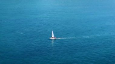 Yelkenlinin açık mavi bir denizde beyaz dalgalarla yüzüşünü gösteren hava görüntüleri. Drone 'dan deniz burnu. Seyahat videosu