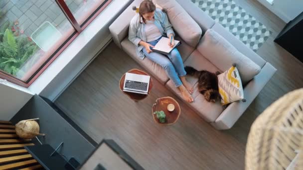 Pandangan Atas Wanita Menulis Catatan Dan Mendengarkan Ceramah Berbaring Sofa — Stok Video
