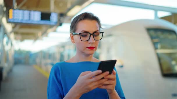 妇女站在一个公共交通站 使用智能手机 等待火车 慢动作 — 图库视频影像