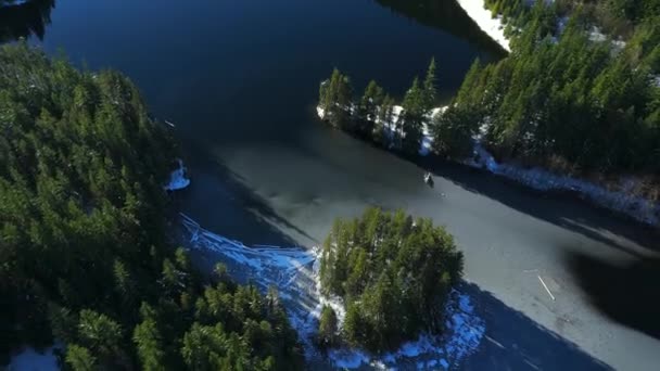 山の中の緑の木や湖を眺める空撮り カナダのブリティッシュコロンビア州の雪で覆われたカナダの岩山の風景 ストック映像